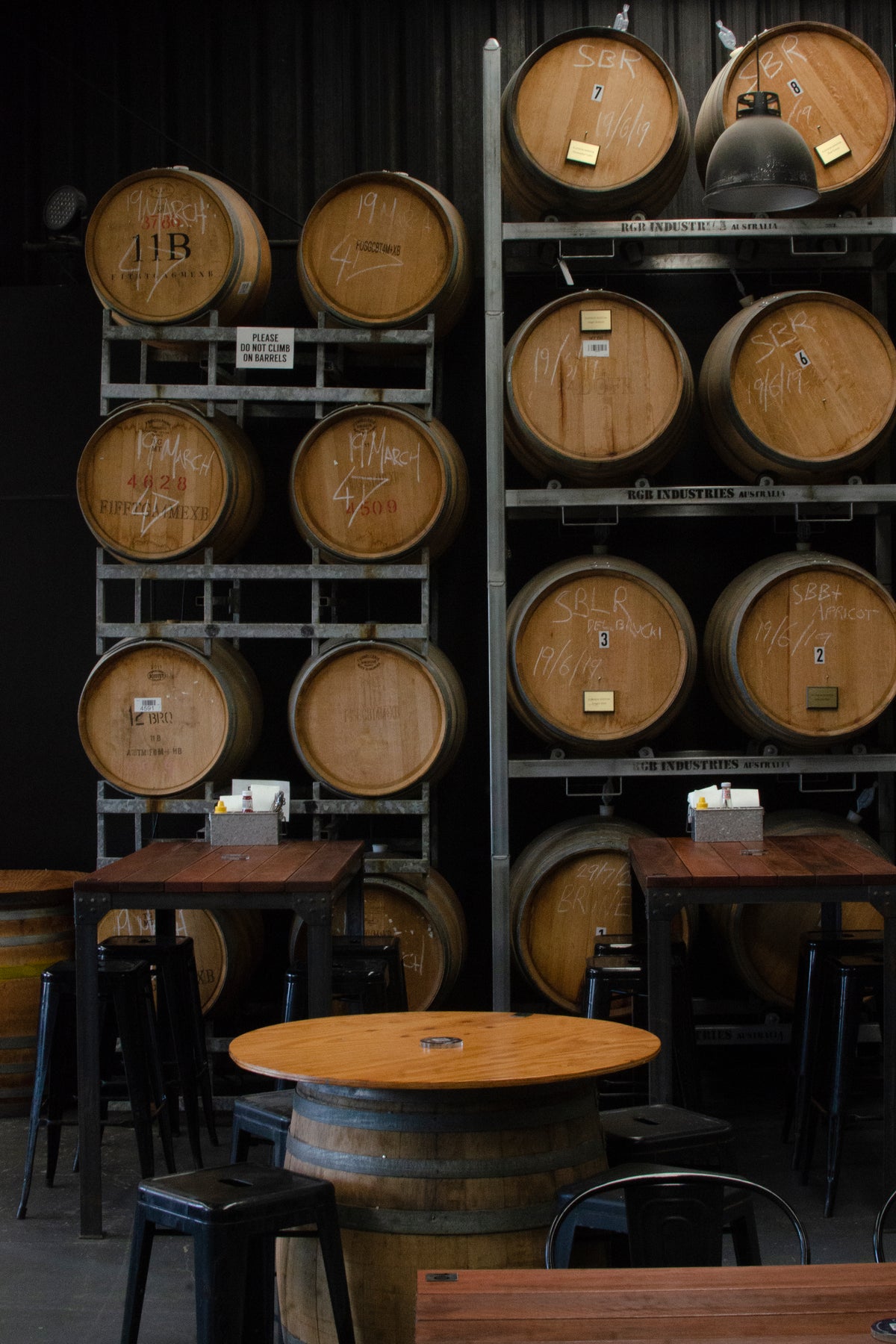 Inside the taphouse: chalk-marked barrels on steel racks above timber tables